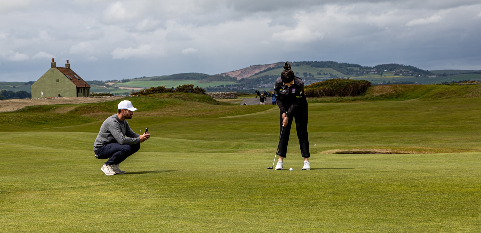 Golfer putting while a coach photographs the course